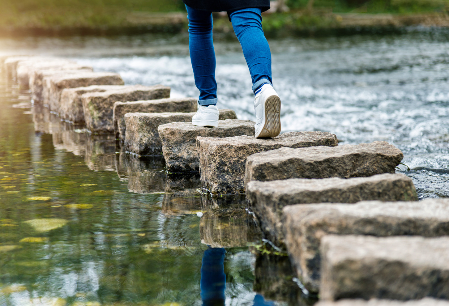 femme qui traverse une rivière par petits pas en montant sur des pierres